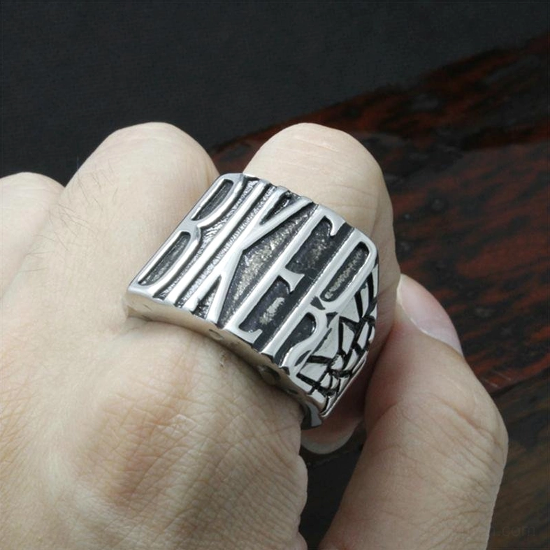 Gothic biker ring worn on human finger, side hand view displaying vintage silver design on dark wooden background
