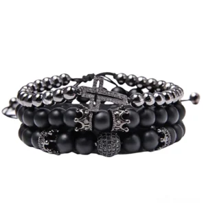 Black gothic charm bracelet set with matte stone beads, ornate cross pendant, and crown charm, flat lay on white background