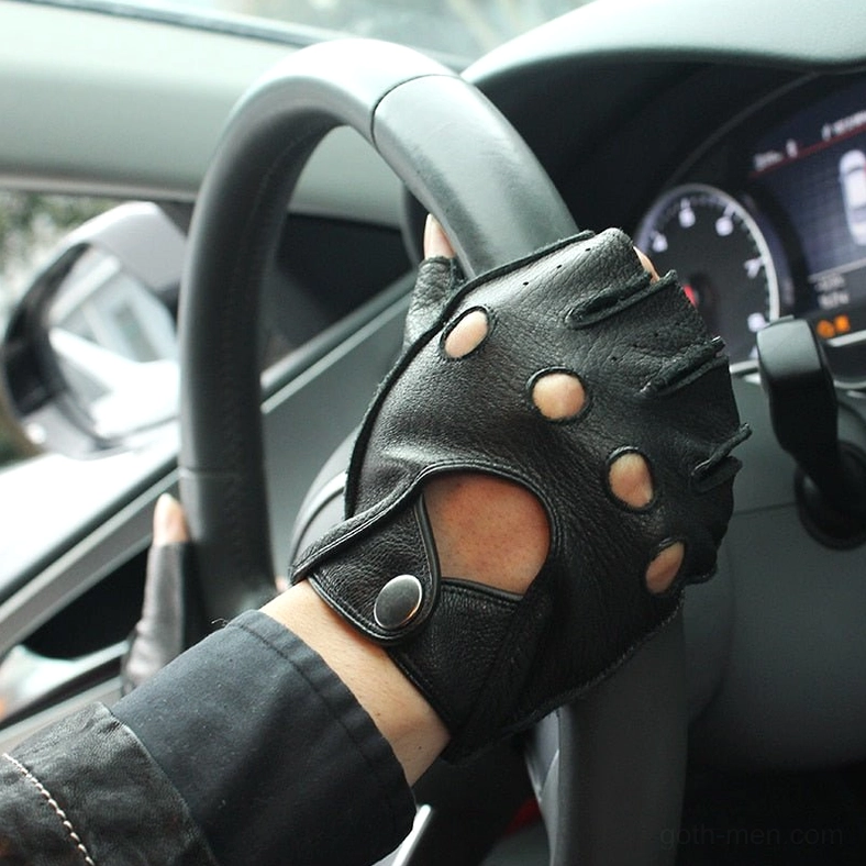 Black fingerless leather gloves with snap closure worn on male hand inside car, driving position