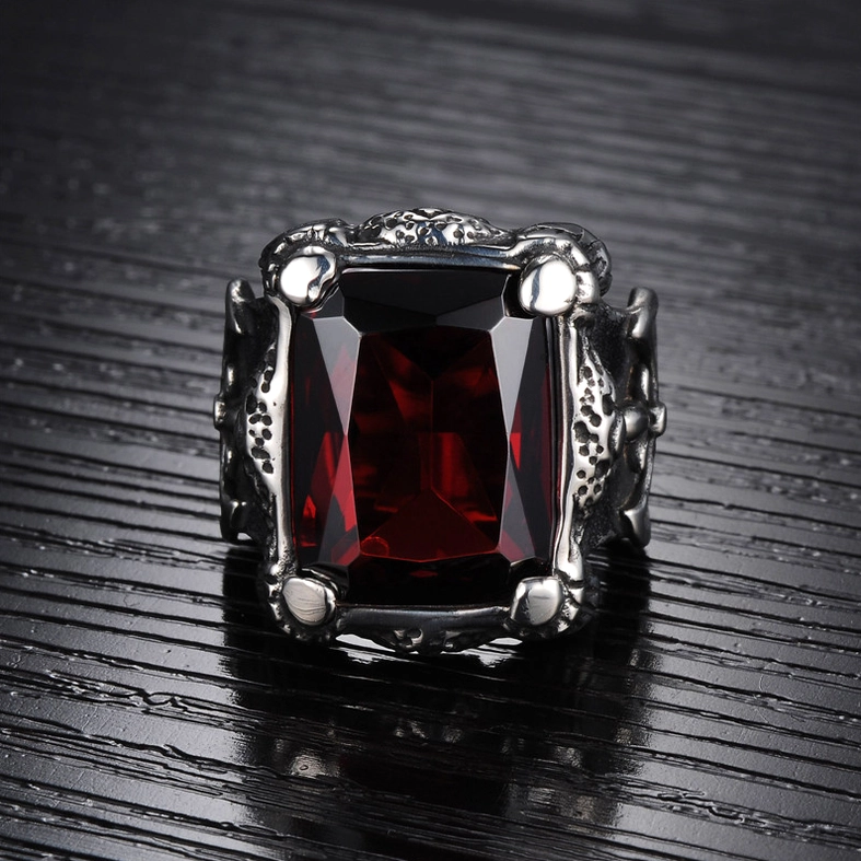 Flat top-front view of blood red zircon ring on wood grain background, highlighting four-claw gem fixation and textured Gothic metal body construction