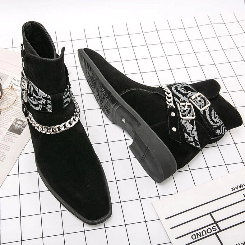 Black faux suede gothic ankle boots flat lay on grid paper with decorative strap and chain hardware visible