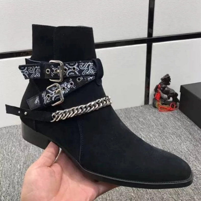 Hand-held side profile of black gothic ankle boots indoors showing paisley buckle chain accents in home setting