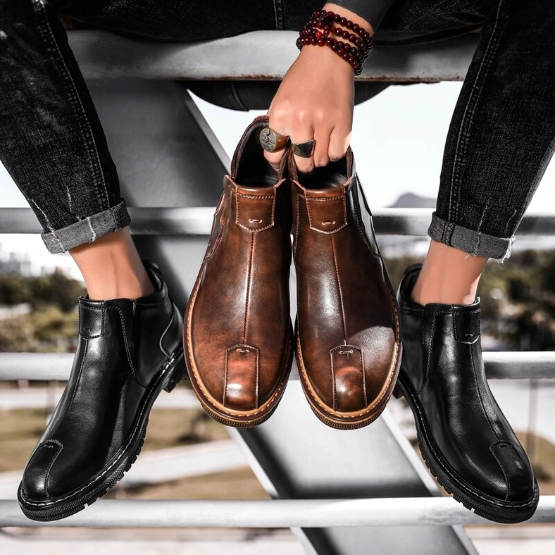 Two-color gothic ankle boots for men held by hand with bracelet, overhead view, black and brown Chelsea style
