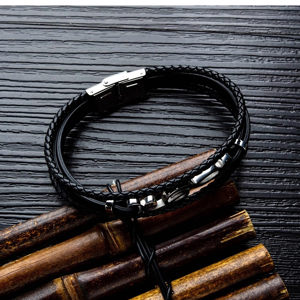 Multi-strand braided black leather bracelet flat lay on dark wood bamboo background with metal hardware stainless steel clasp gothic mens accessory