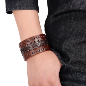 Brown gothic braided leather wide cuff bracelet worn on wrist with denim background, showing cross-woven texture and snap closure detail