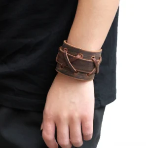 Gothic vintage brown genuine leather cross-lace wristband bracelet worn on male arm, side view showing distressed texture and adjustable metal buckle detail