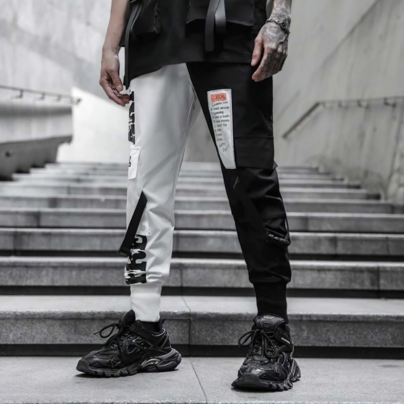 Front low-angle shot of gothic patchwork cargo pants with graphic prints and side utility straps on stairs