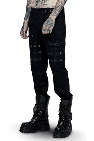 Front three-quarter view of black gothic cargo pants with multi-grommet side pockets on tattooed male model wearing skull-button hardware