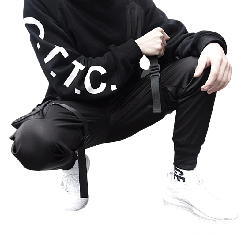 Techwear cargo pants worn by male model in squatting position showcasing strap decorations and fitted ankle design with white sneakers