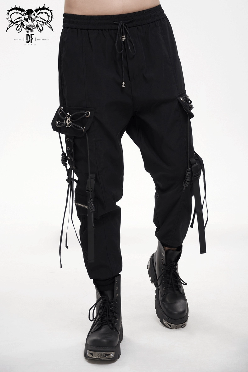 Three-quarter front angle of black gothic cargo pants on model displaying hanging tactical straps and pentagram accents