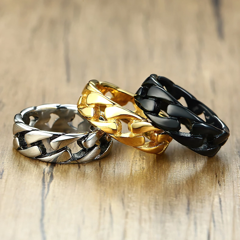 Gothic chain ring collection flat lay - black, silver, and gold stainless steel curb rings on wooden surface