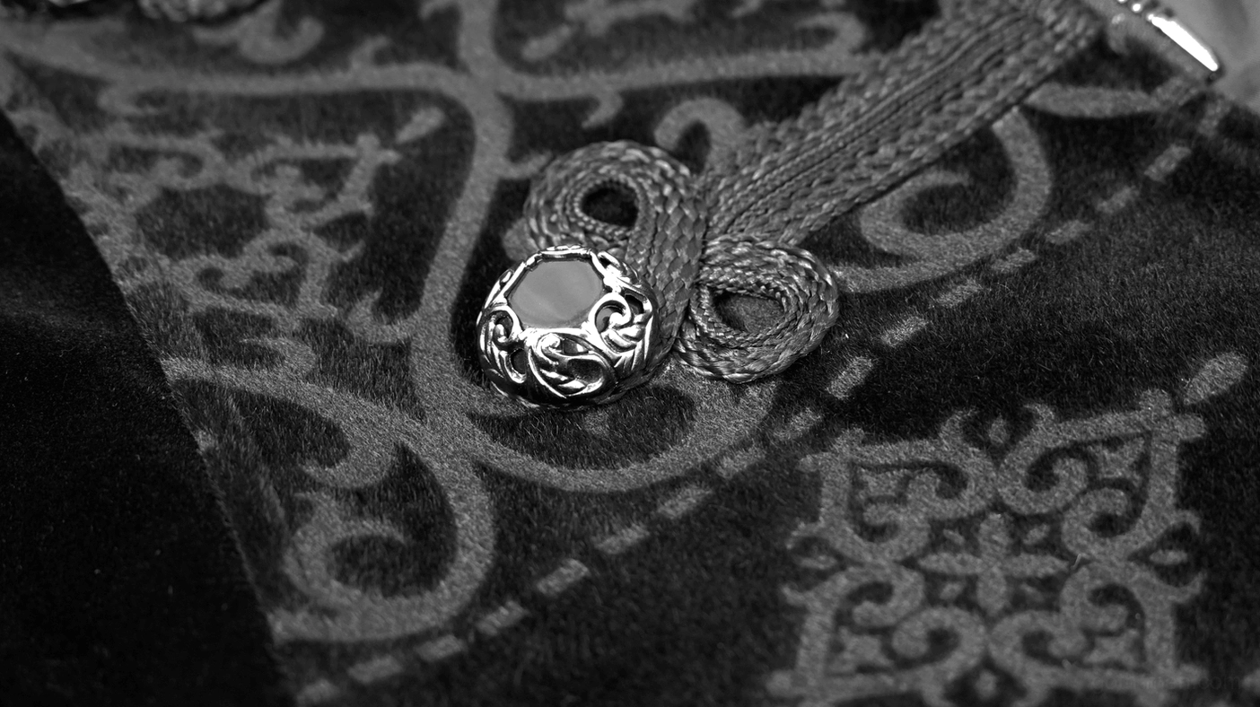 Macro shot of black gothic velvet coat engraved silver decorative button on embossed fabric