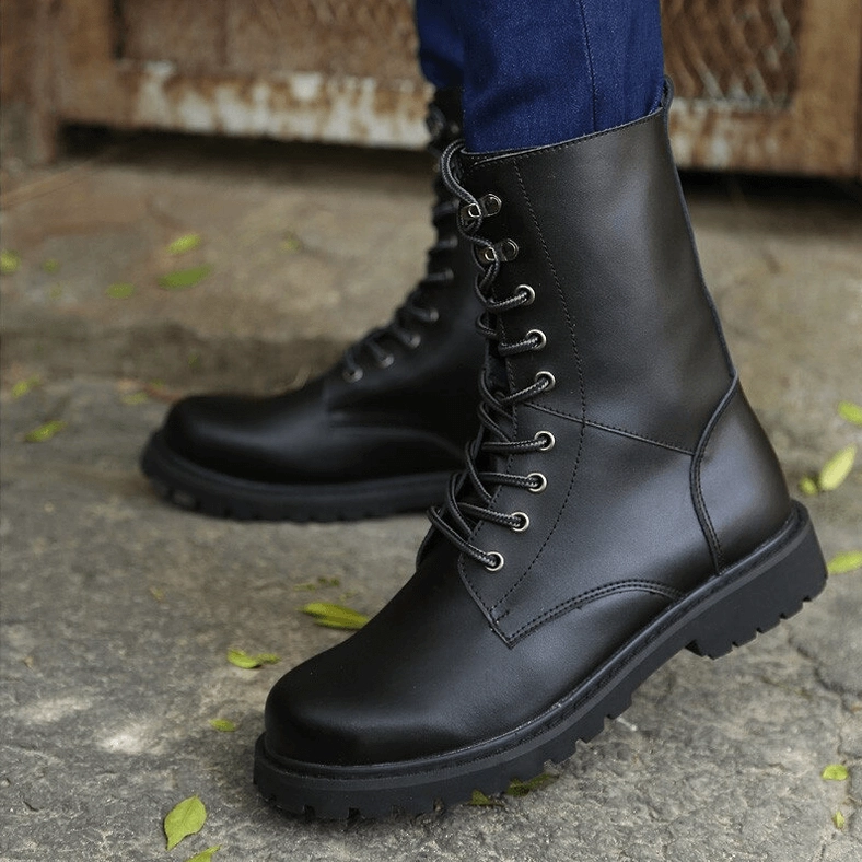 Black combat boots on model wearing blue jeans, low side-view of thick rubber outsole on stone pavement outdoor setting