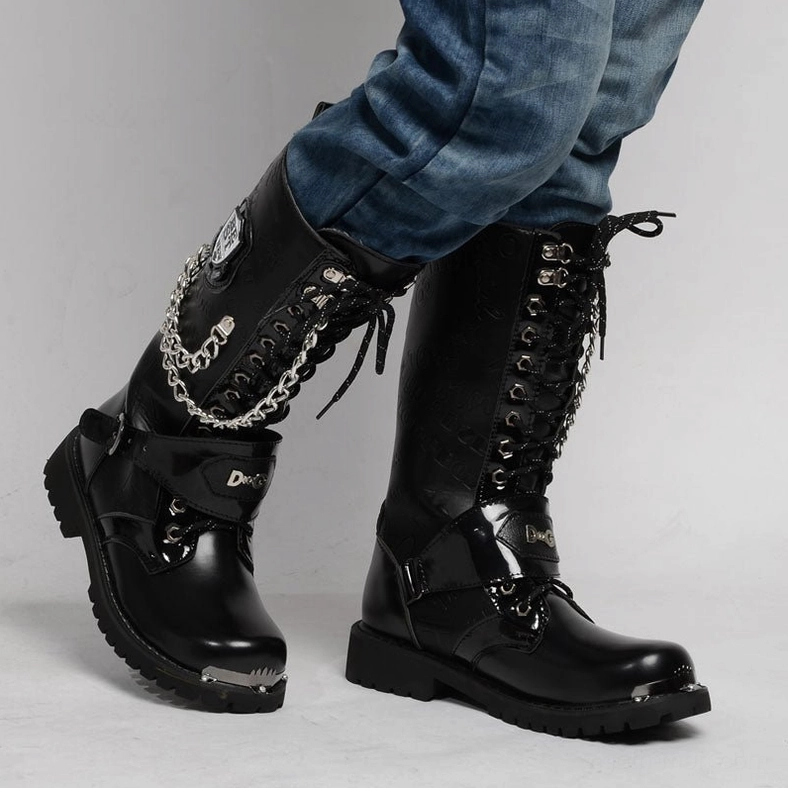 Model wearing black gothic combat boots styled with blue denim jeans, three-quarter angle view showing tactical buckles and chain decorations