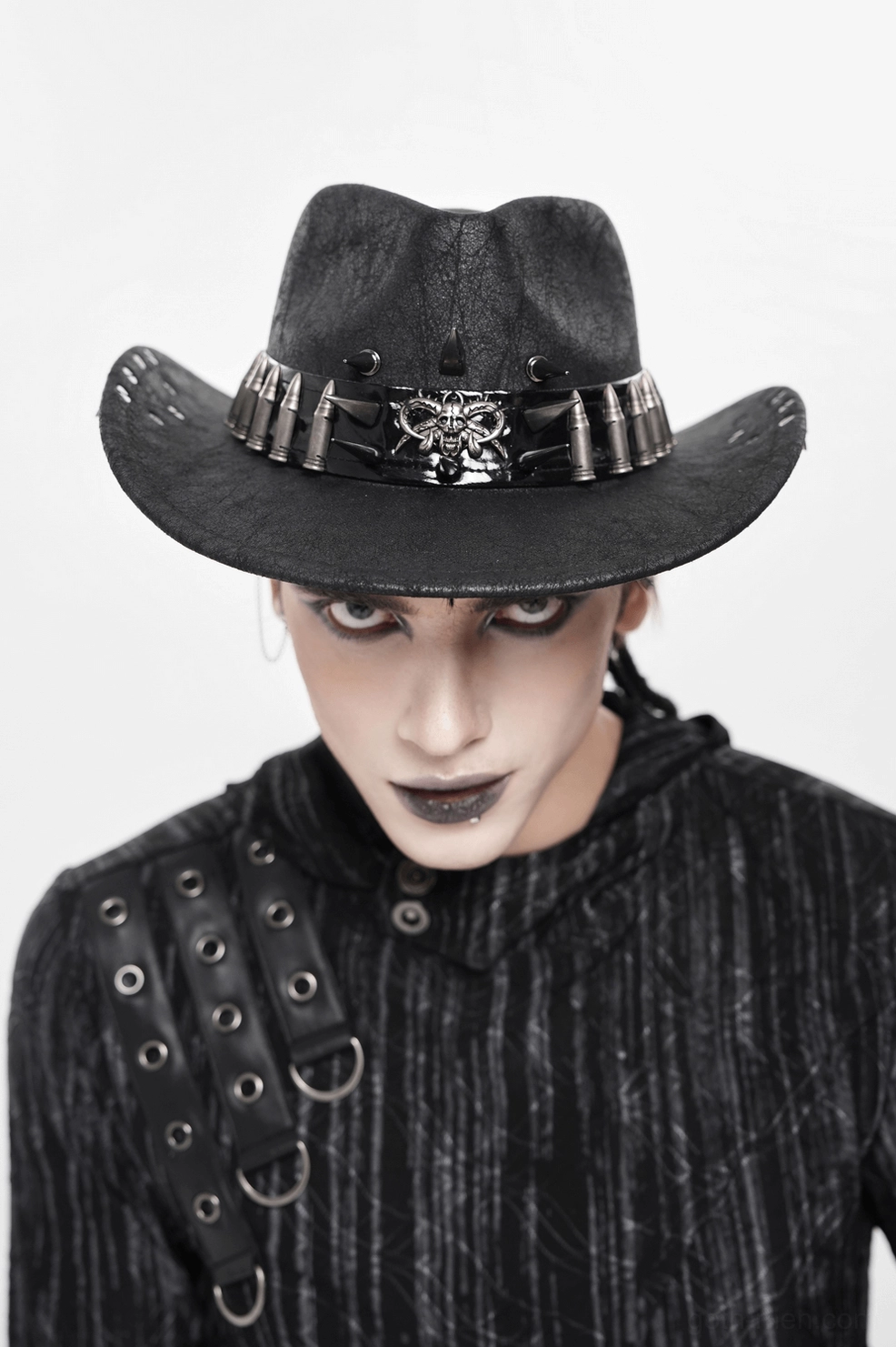 Front angled view of black gothic cowboy hat with metal skull and bullet band worn by goth styled male model