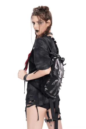 Goth style model in dark outfit wearing gothic demon backpack side profile view, pure white background, alternative fashion styling with distressed clothing