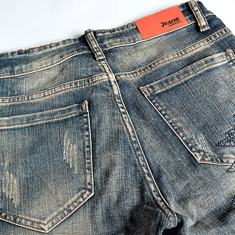 Rear closeup of vintage blue denim jeans showing back pockets, branded leather tag, and distressed finish on gothic embroidered denim