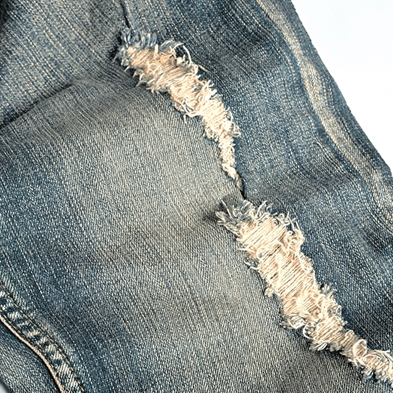 Macro closeup of frayed ripped denim fabric texture showing vintage blue wash, worn distressing effects, and fabric edges detail