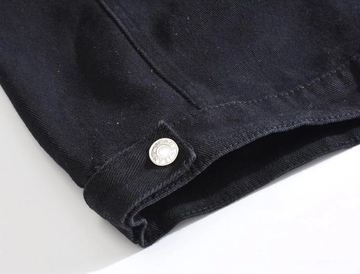 Close-up of black denim vest hem showing metal adjustment button and twill texture