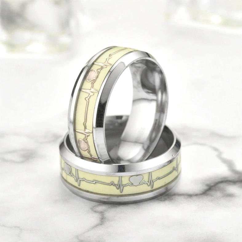 Luminous stainless steel ECG heartbeat couple rings with cream inlay on marble surface, overhead view