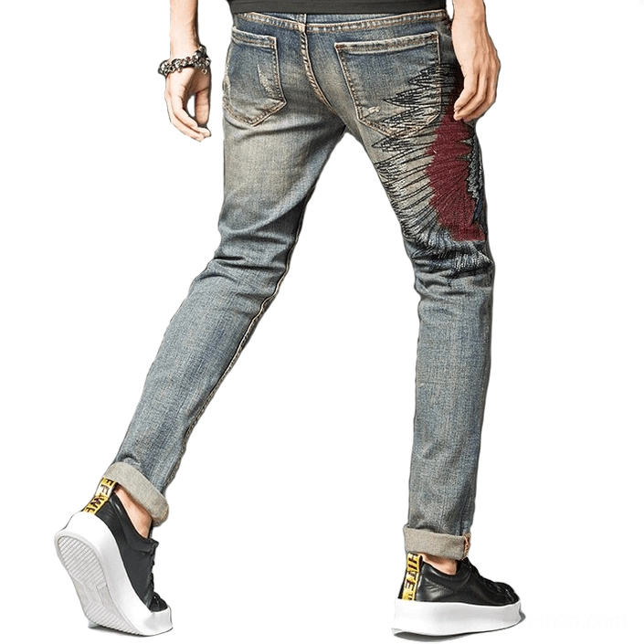 Rear view of alternative gothic ripped denim jeans for men, featuring back embroidery details, cuffed ankles, and vintage blue wash distressing