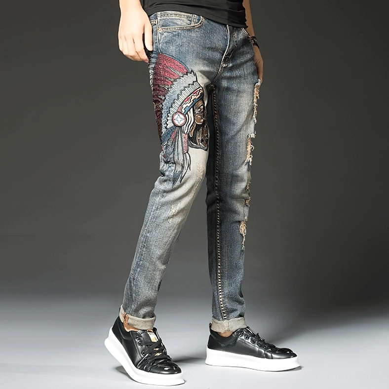 Side profile of gothic embroidered denim jeans for men featuring Indian chief embroidery motif, frayed rips, and vintage blue wash