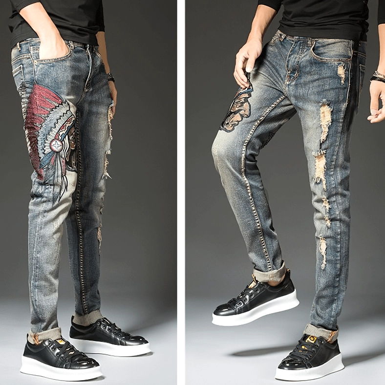 Three-quarter rear view of alternative men's embroidered ripped denim jeans showing cuffed ankles, pocket details, and distressed finish