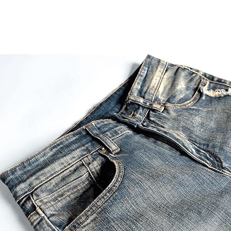 Front three-quarter view of men's gothic ripped denim jeans with embroidered thigh patch, vintage blue wash, and strategic distressing