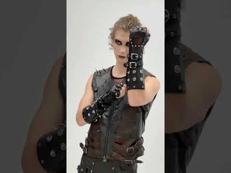 Male goth cosplayer wearing black fingerless leather gloves with metal studs and buckle straps, front view showcasing alternative fashion styling