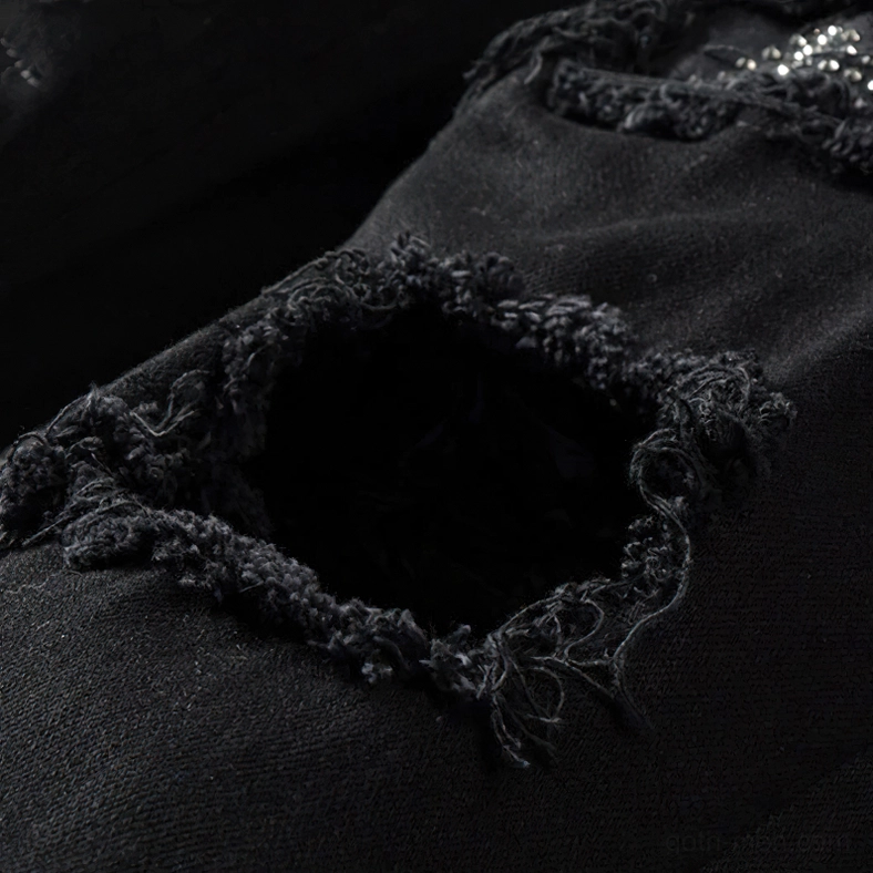 Frayed ripped denim hole showing destruction detail on gothic style black jeans