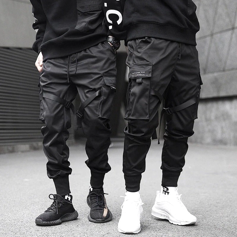 Two male models in black cargo joggers on concrete street showing rear silhouette of tapered cuffs and relaxed fit through thighs