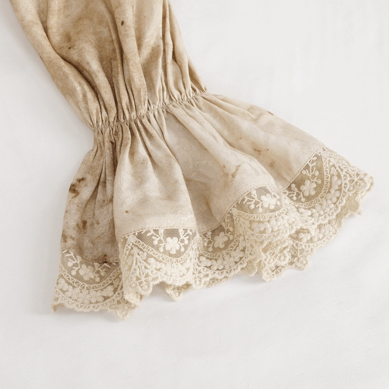 Close-up detail of lantern sleeve cuff showing elastic ruched trim and embroidered lace detailing on distressed jacquard fabric