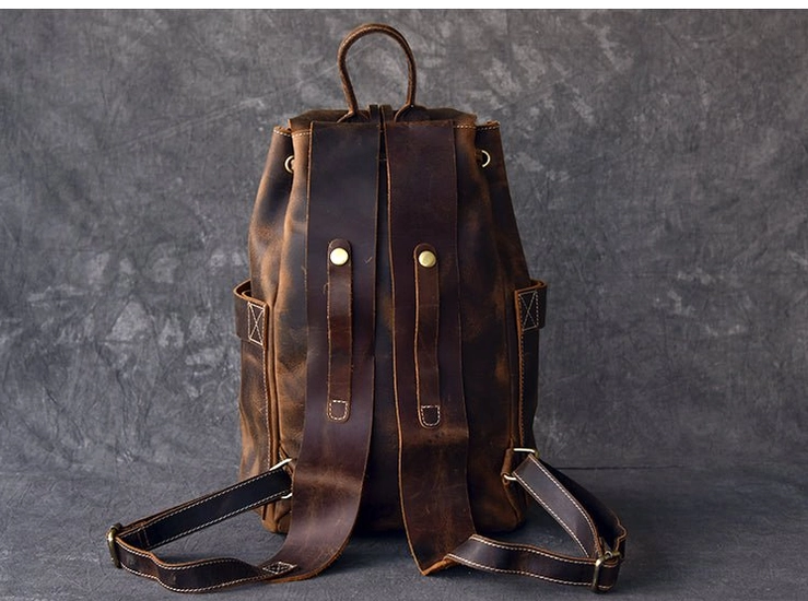 Close-up of brown leather gothic travel backpack showing embossing and decorative belt straps with metal rivets