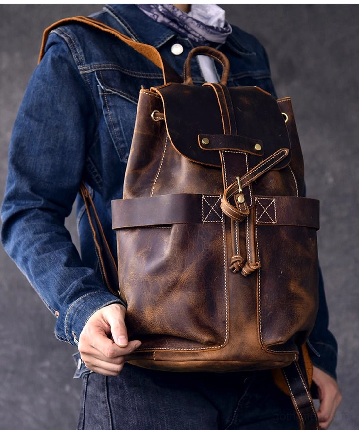 Front three-quarter shot of genuine brown leather gothic backpack held by male model in denim