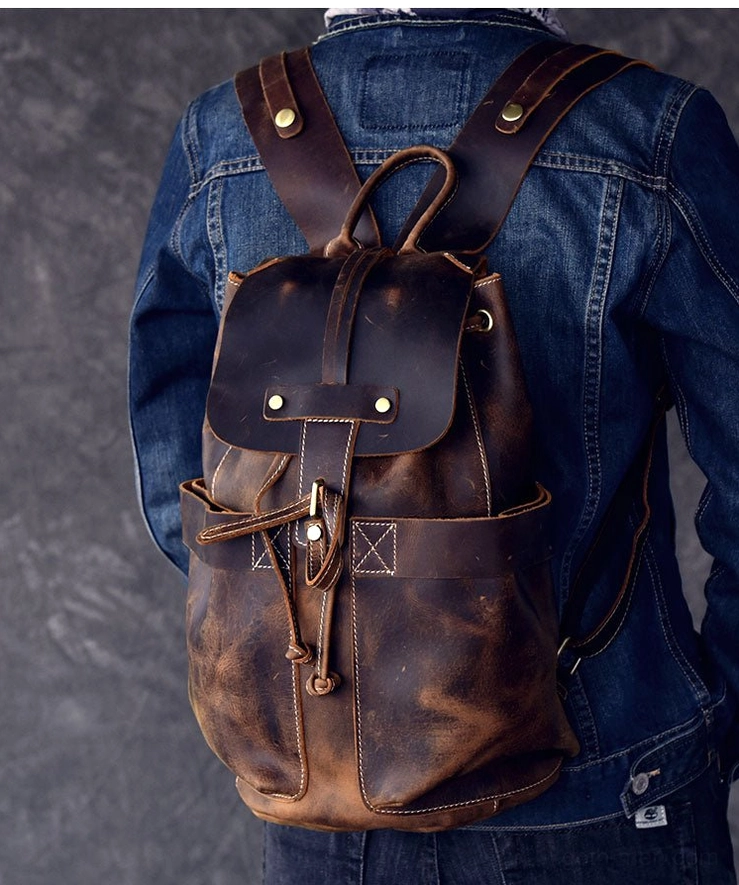 Back three-quarter view of dark gothic leather travel backpack on male model showing drawstring and flap design