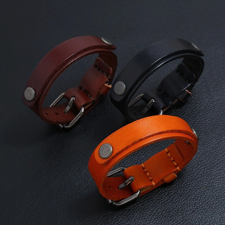 Three-piece collection of genuine leather gothic bracelets in black, dark brown, and tan with rivet and buckle detailing, overhead view