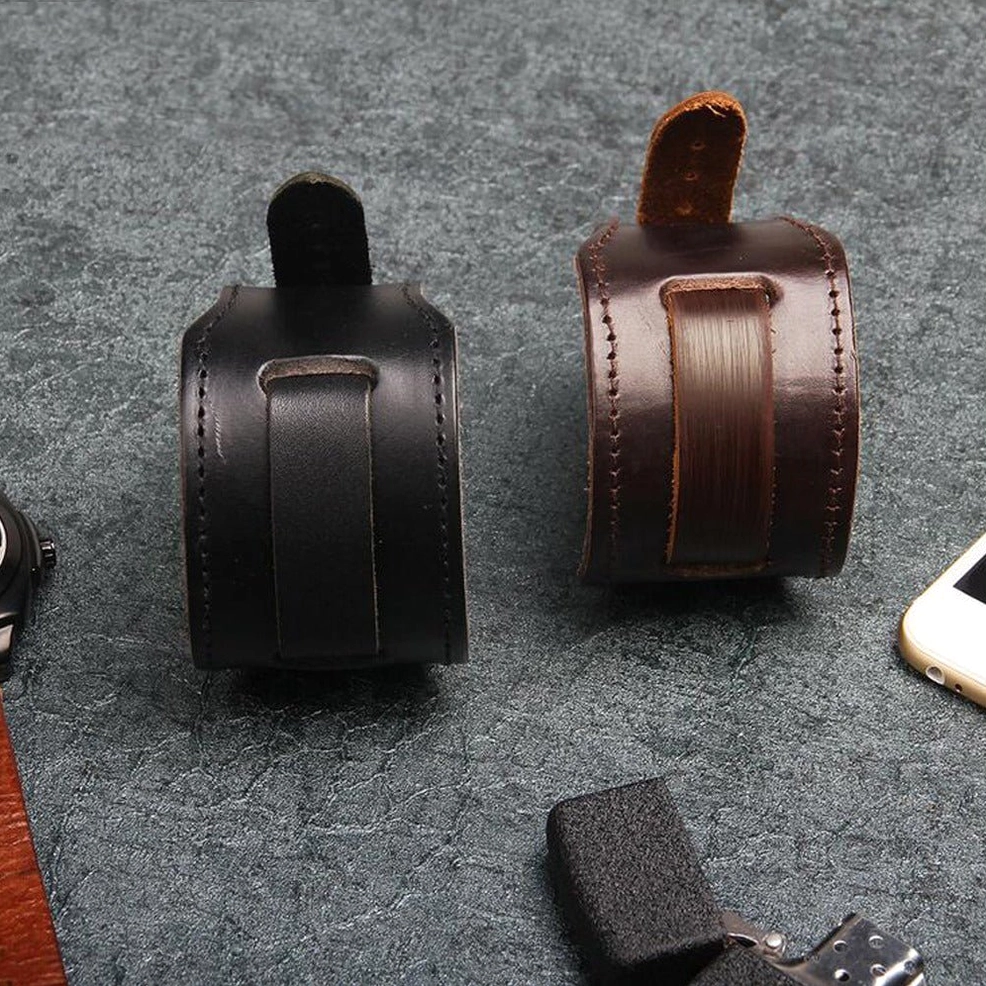 Flat lay comparison of black and brown leather gothic cuff bracelets on dark textured desktop with lighter and smartphone