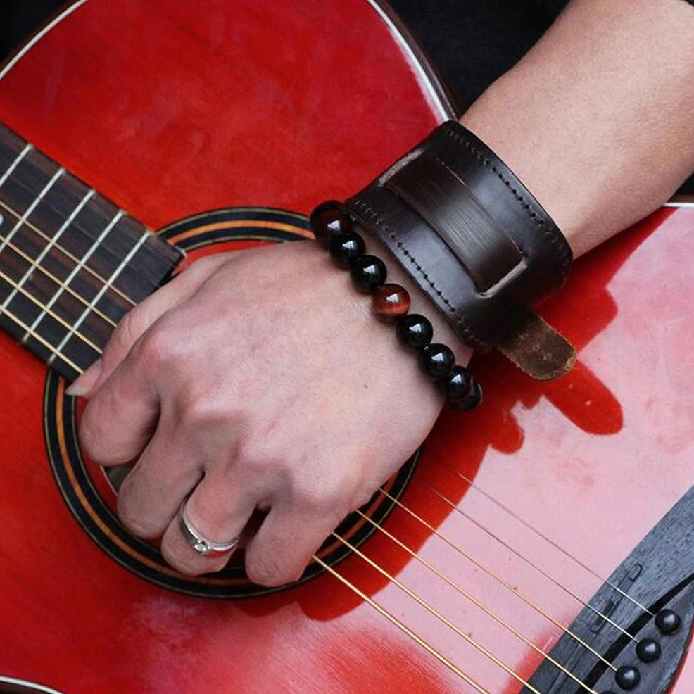 Male hand wearing dark brown leather gothic cuff bracelet on wrist, styled next to red acoustic guitar, side profile shot