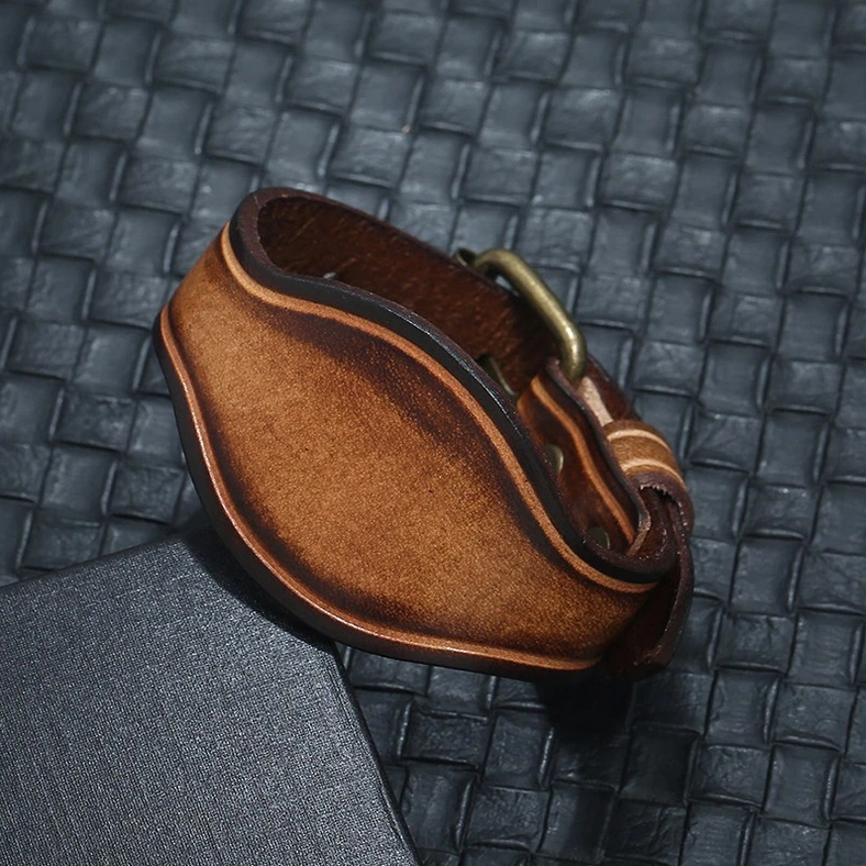 Distressed leather wristband with brass hardware shown from top-down side angle displaying vintage patina and edge craftsmanship
