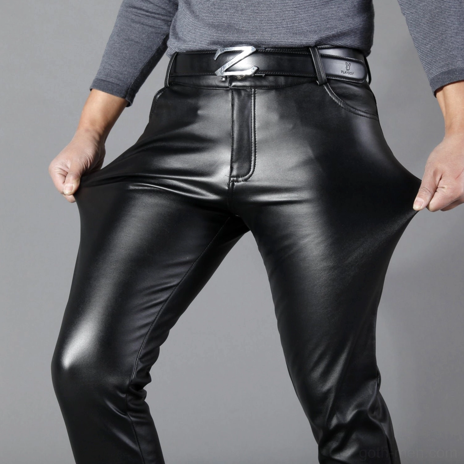 Close-up detail of men's black gothic leather pants showing Z-shaped belt buckle and glossy faux leather texture elasticity demonstration