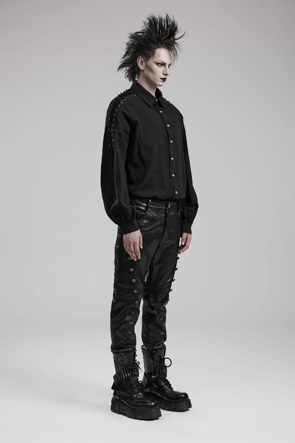 Rear profile of black studded gothic leather pants on model highlighting studded waist belt and slim tapered leg
