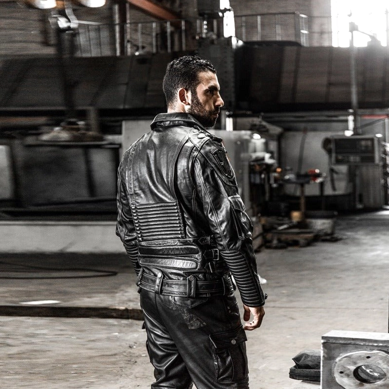 Male model wearing black genuine leather gothic motorcycle jacket from behind, padded back panel visible, waist adjustment buckles, rear silhouette