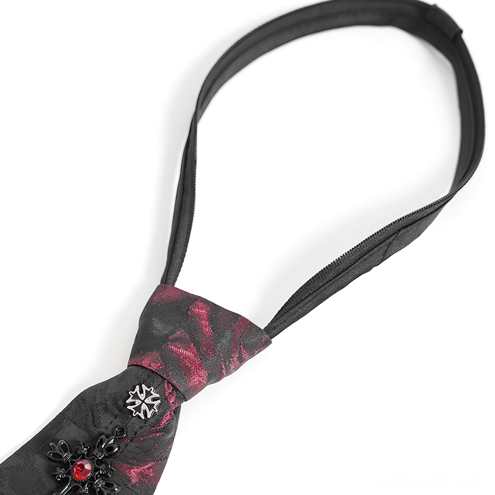 Close-up flat lay of black and red rose gothic necktie showing red rose jacquard fabric, black cross with red gem center, and silver stud details