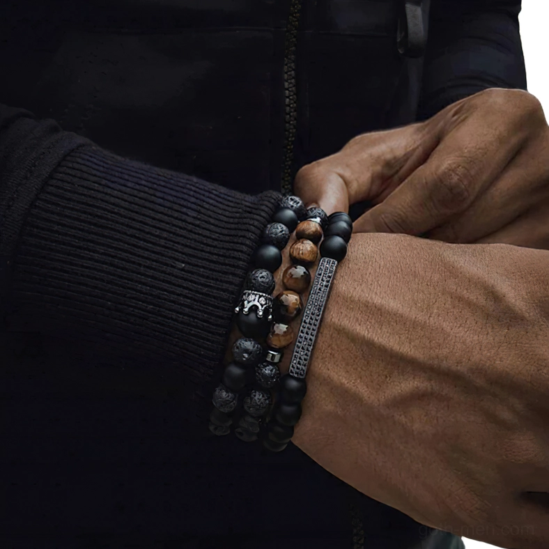 Alternative mens black onyx stone bracelet with tiger eye accents and crown charm worn on dark-skinned wrist, front close-up shot gothic aesthetic