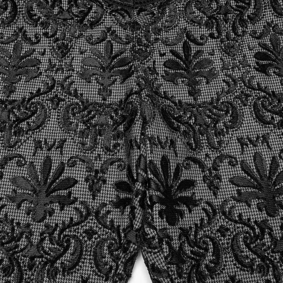 Macro close-up of fleur-de-lis damask lace pattern on black mesh base of gothic embroidered pants