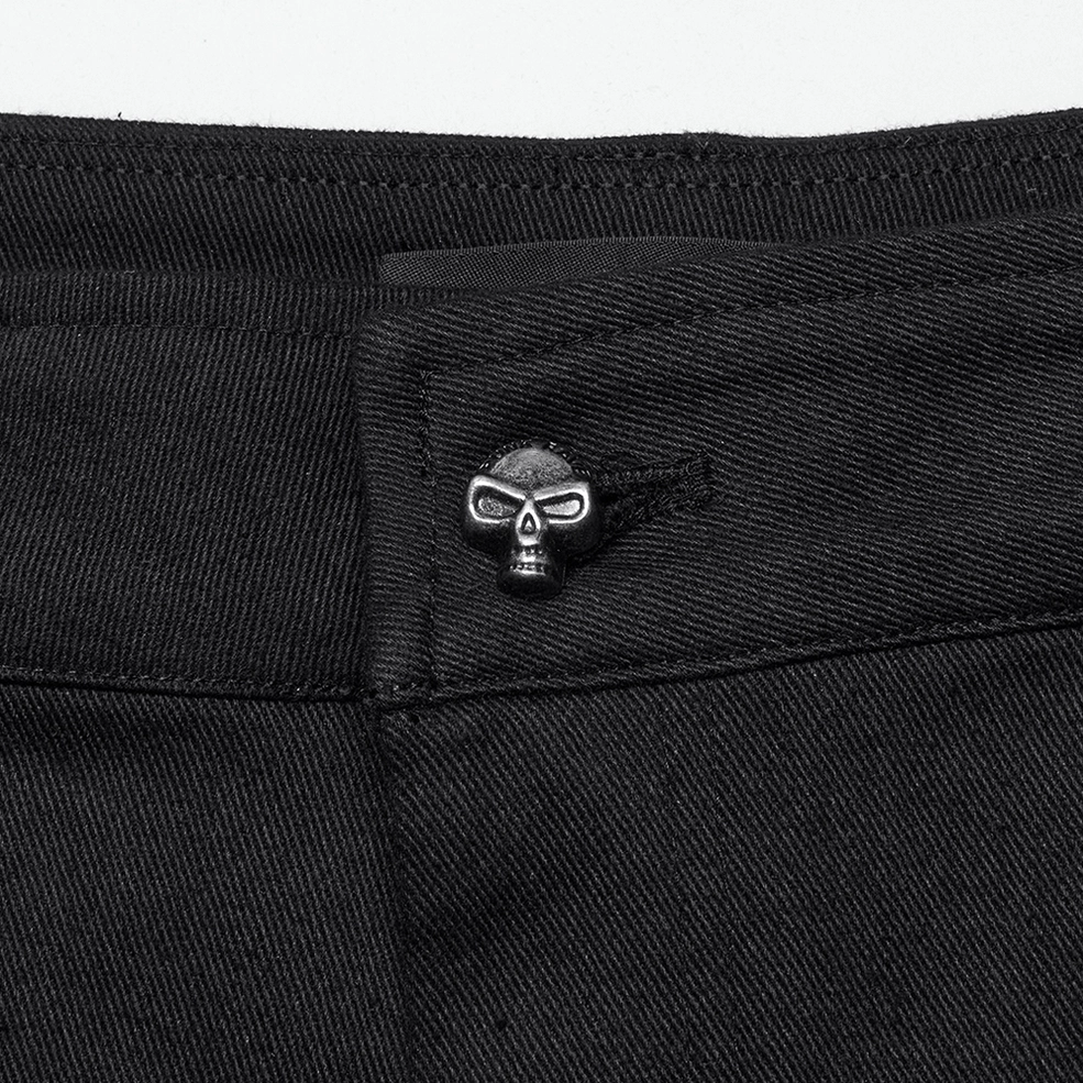 Close-up detail of skull-shaped metal button and black twill waistband stitching on gothic pants