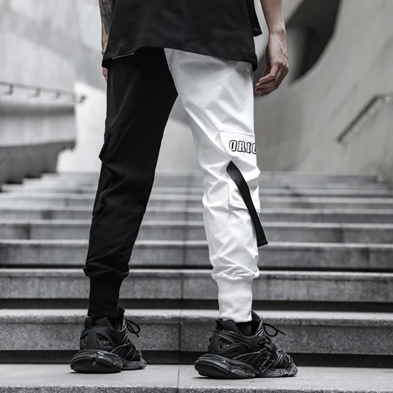 Back medium shot of men's black and white split color cargo pants with patch text labels and utility details