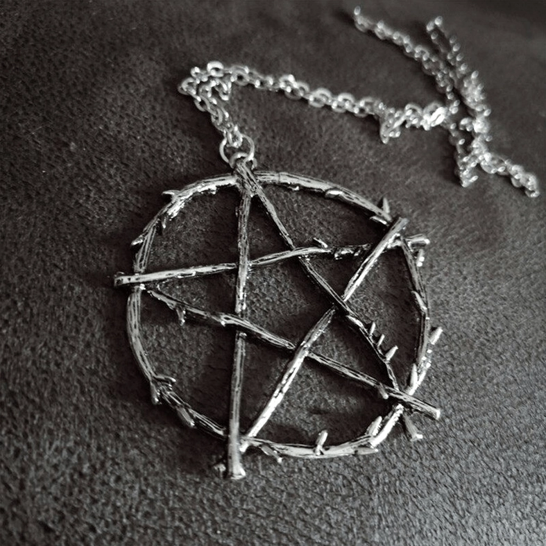 Overhead close-up of dark vintage gothic pentagram necklace laid on leather background, showing complete chain and pendant with thorn-like details