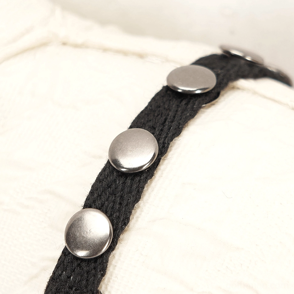 Detailed shot of black canvas harness with round metal studs and rivets on gothic plush ornament