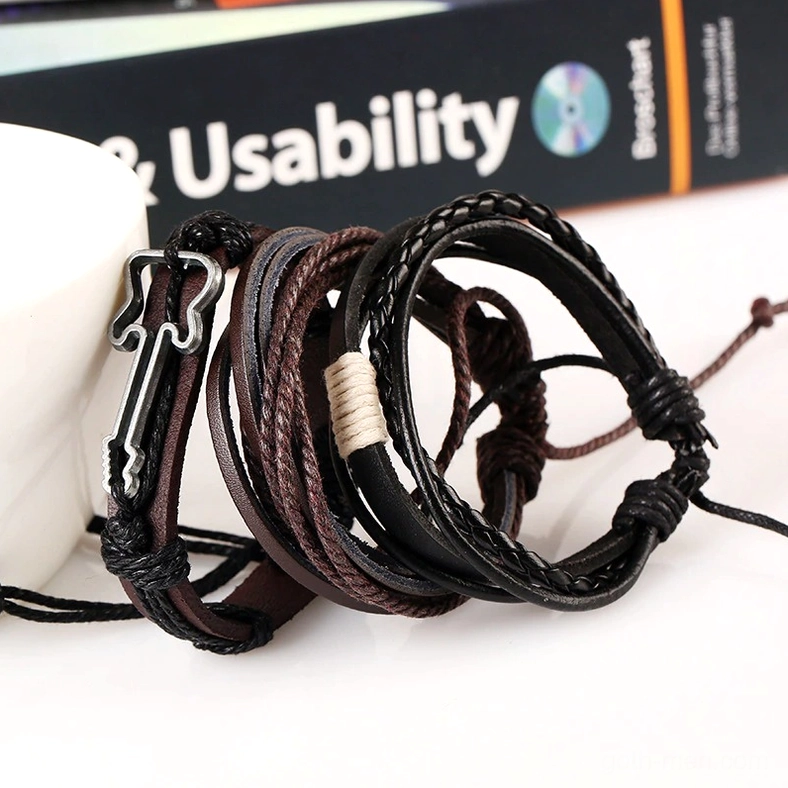Gothic punk bracelet close-up showing mixed brown and black genuine leather construction, braided cord texture, and iron alloy guitar charm with antique silver plating on tabletop with book background